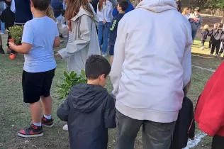 Alumne de Batxillerat amb alumnes d'infantil al pati de l'escola agermanats per a celebrar la Pasquan fent una plantada al pati de l'escola