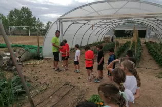 Nens i nenes de 2n de primària a l'hort de la granja escola de La Manreana escoltant les explicacions del monitor del taller